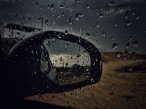 Vidro do carro e retrovisor molhado. Imagem ilustrativa do texto sobre chuva ácida no vidro.