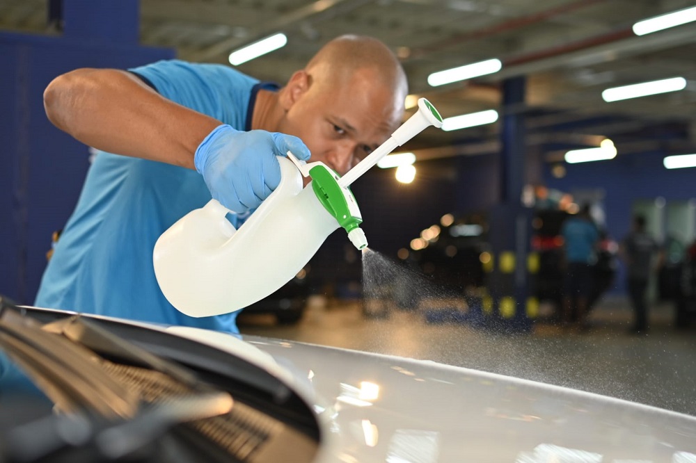 Imagem de um técnico da Acquazero usando uma blusa azul clara borrifando um líquido na lataria de um carro cinza. Imagem ilustrativa texto como é feita a lavagem a seco.
