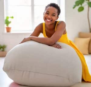Mulher sorridente, usando vestido amarelo, enquanto se apoia em um puff. Ilustração do texto sobre como limpar puff de tecido.