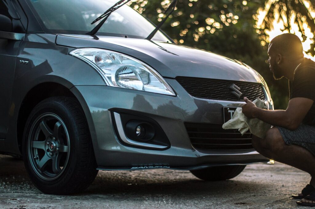 Homem limpando carro cinza com uma flanela. Imagem ilustrativa do texto sobre lavagem a vapor automotiva.