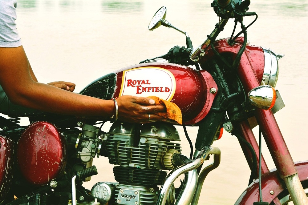 Imagem de uma mão passando um pano amarelo em uma moto com a carenagem na cor vermelha. Imagem ilustrativa texto lavagem detalhada moto.