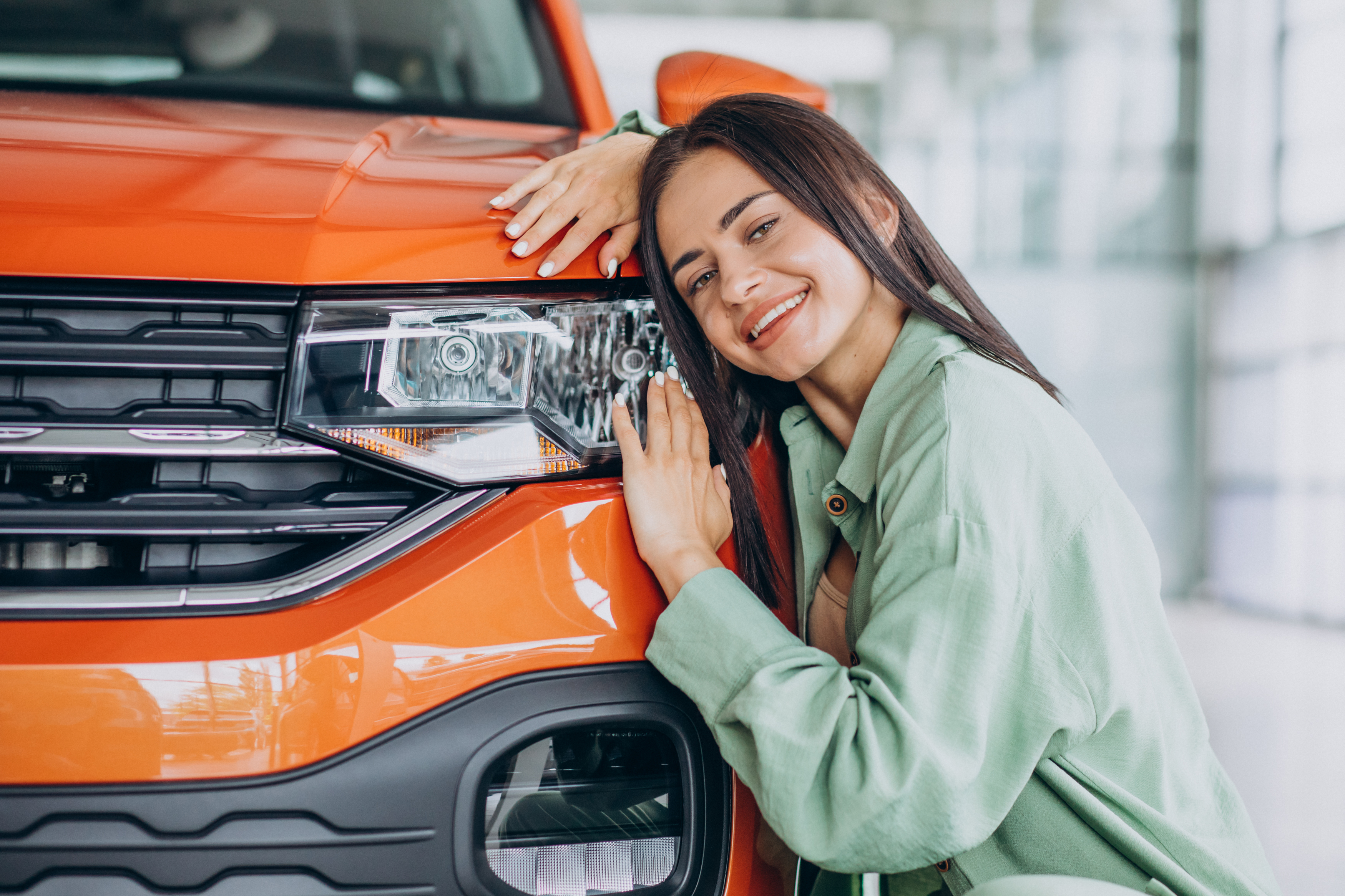 Mulher agachada abraçando a frente de um carro laranja e sorrindo imagem ilustrativa do texto sobre vender carro