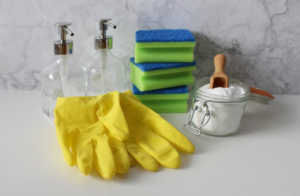 kit de limpeza com três esponjas azuis e verdes, bicabornato,  dois recipientes vazios e duas luvas amarelas. Imagem ilustrativa do texto sobre como limpar o colchão a seco.