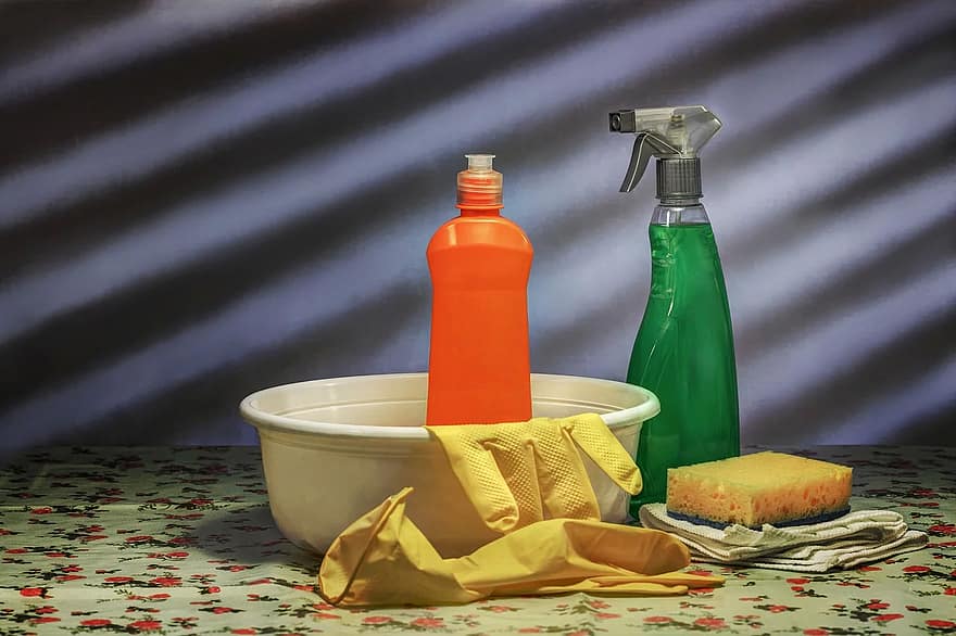 Uma bacia bege e dentro dela uma embalgem laranja e uma luva amarela. No lado de fora, uma embalagem com líquido verde, uma esponja amarela, pano e a outra luva. 