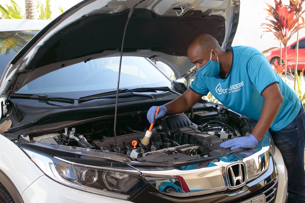 Man wearing Acquazero shirt and technically cleaning the car's engine with a detailing brush; illustrative image text about car wash