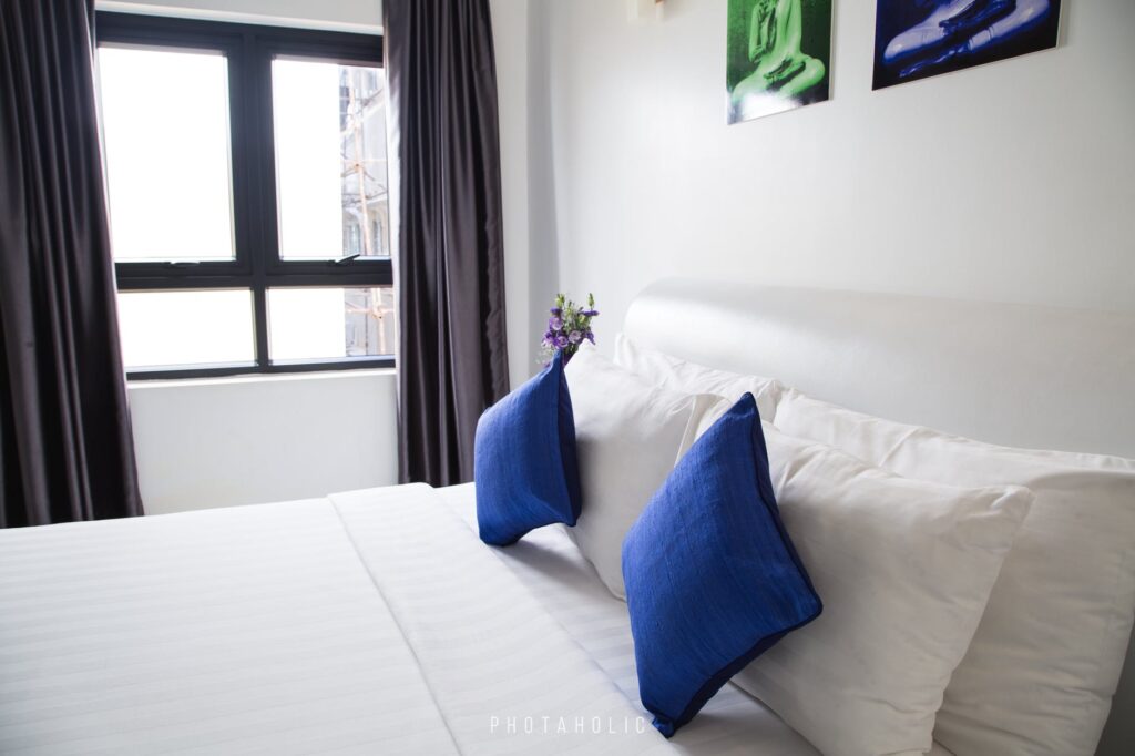 Uma cama com lençóis e travesseiros brancos e duas almofadas azuis. Imagem ilustrativa do texto sobre como tirar manchas de travesseiro.