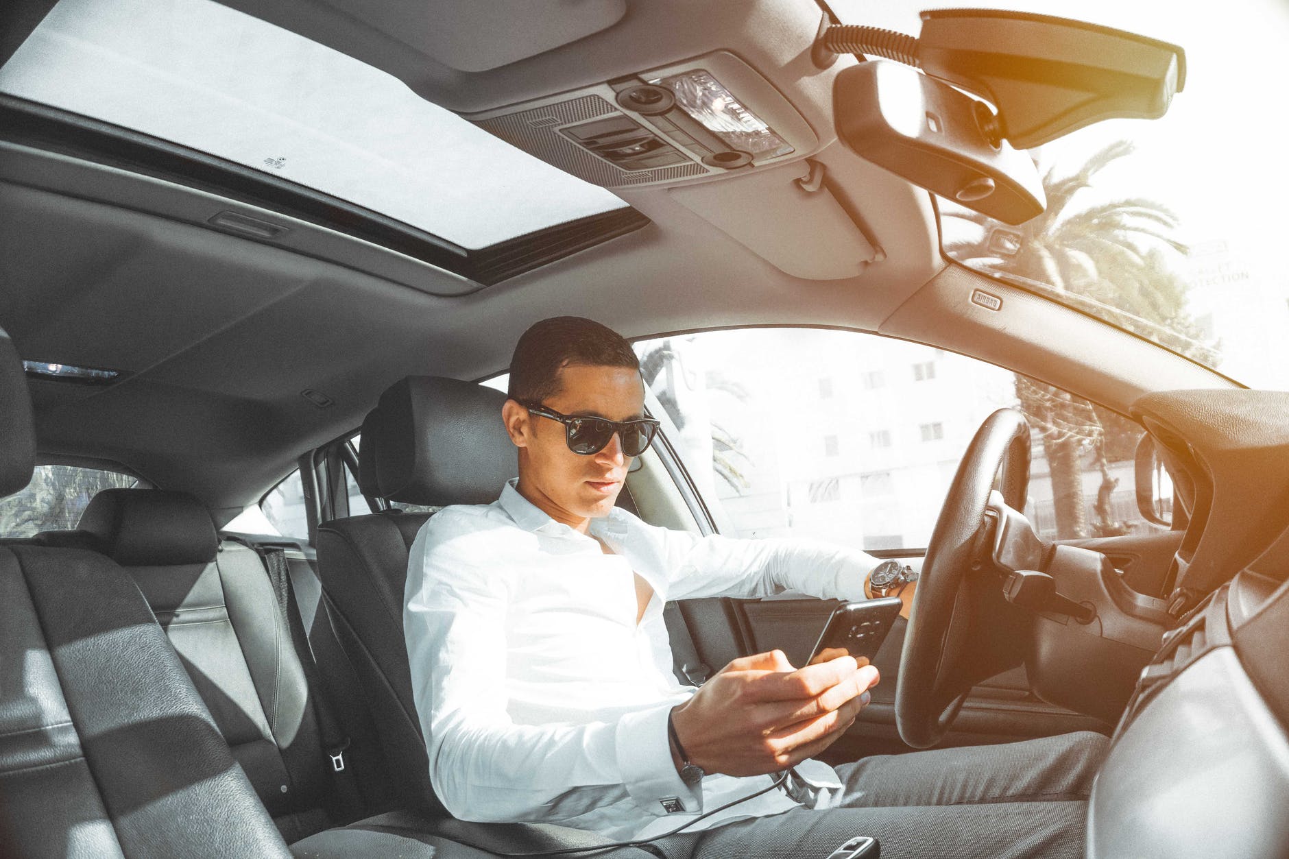 Interior do carro e homem com celular na mão sentado no banco da frente. Imagem ilustrativa do texto sobre limpar seu carro por dentro em casa.