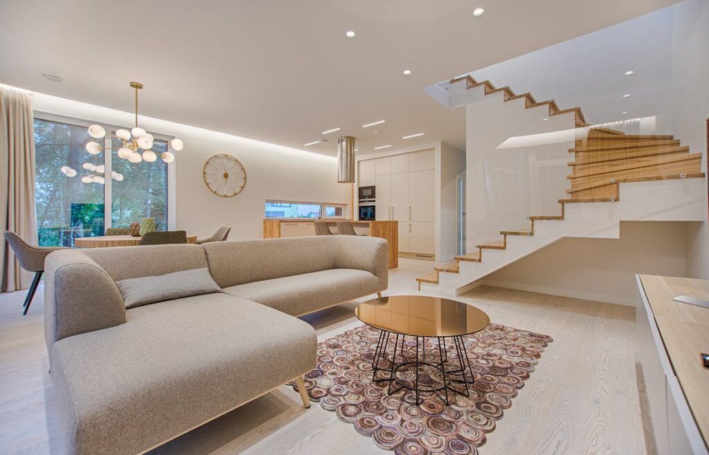 sala moderna em tons claros com mesa espelhada, sofá cinza e escada de madeira.