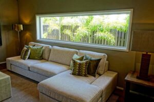 sala com sofá claro e com uma janela comprida com vista para o jardim. Imagem ilustrativa do texto sobre lavagem de estofados.