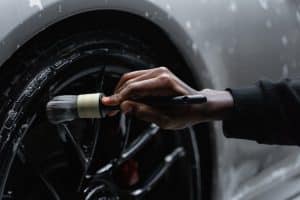 Pessoa passando pincel para limpar pneu de um carro cinza. Ilustração do texto sobre rodas e pneus.